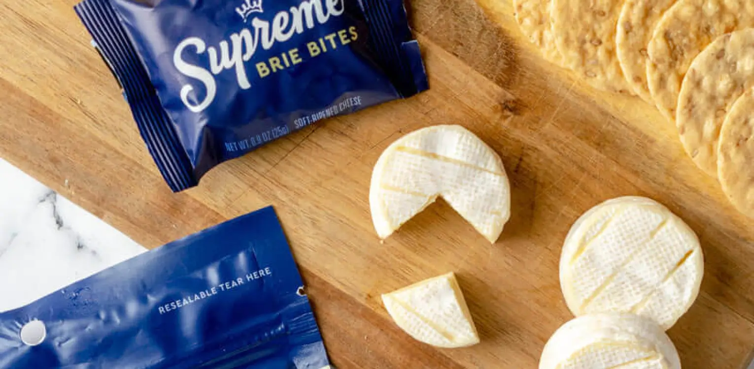 Supreme Brie Bites package and sliced brie cheese on wooden board with crackers.