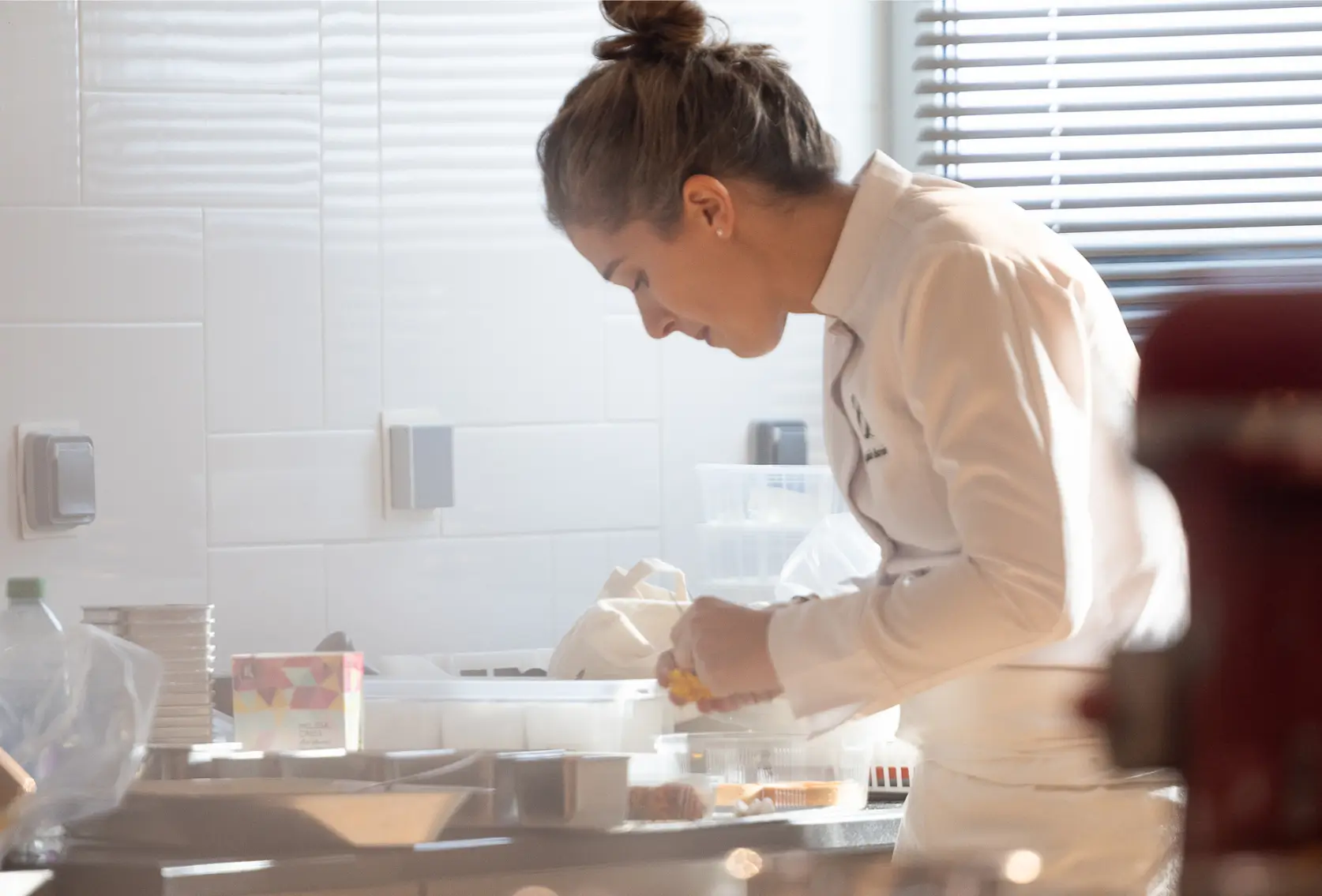 Woman in cream sweater preparing food at kitchen counter with ingredients and containers visible.