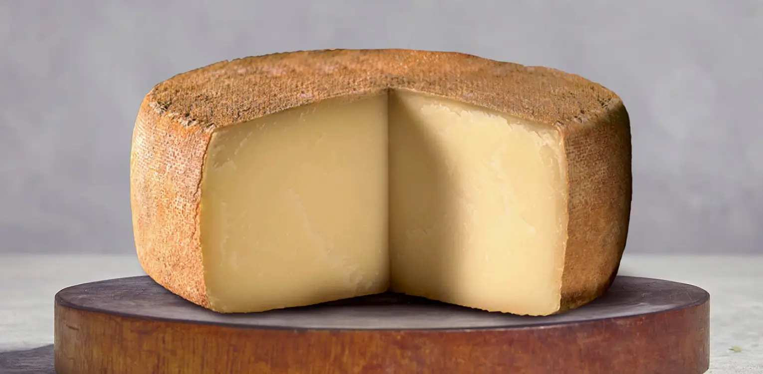 Wheel of aged cheese with golden rind cut to show pale yellow interior, displayed on wooden board.