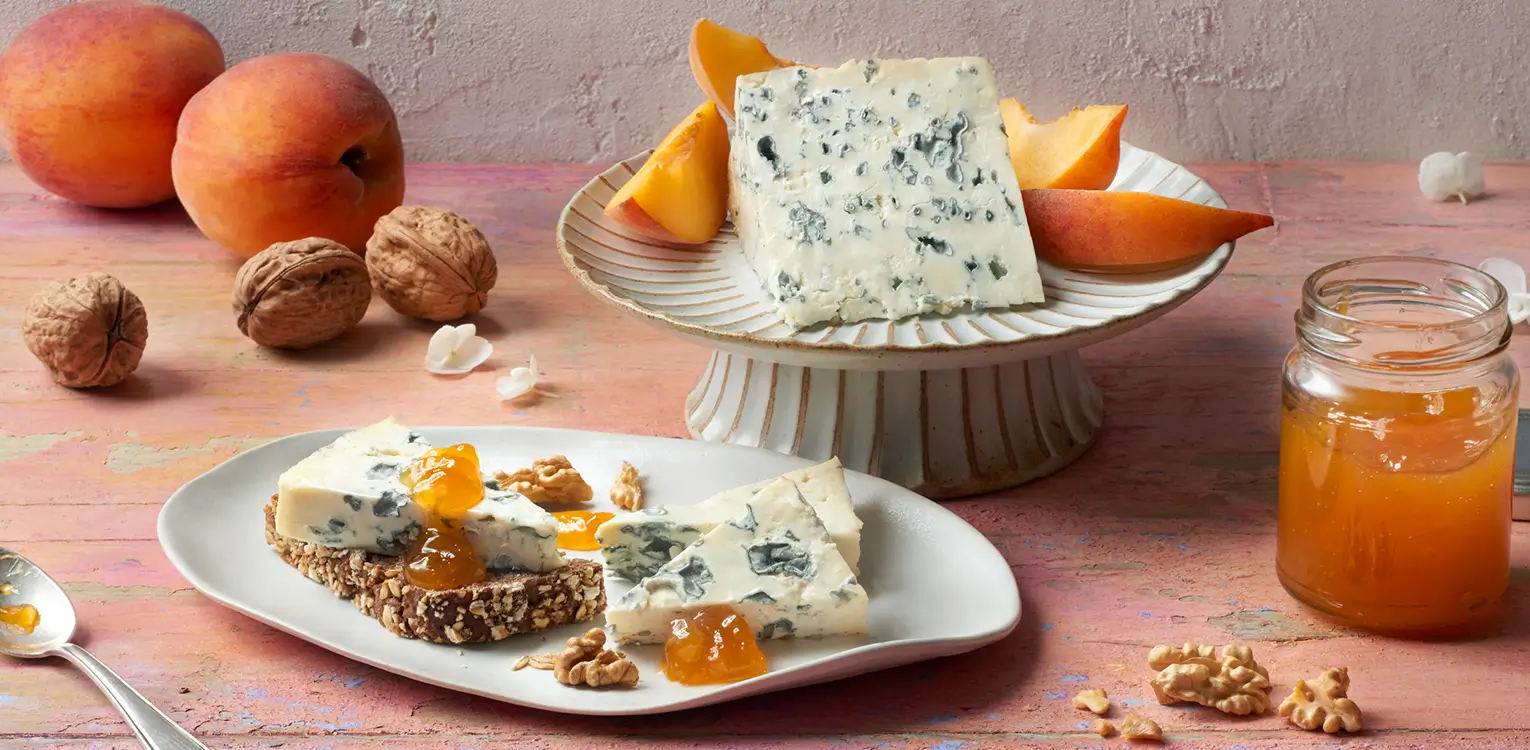 Blue cheese with apricots, walnuts, and honey on a pink wooden table with fresh fruit and ingredients.